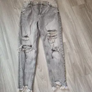 Gråa slitna jeans med hål vid lår och knäskål. De är ankellånga, knappt använda. Tajta jeans.