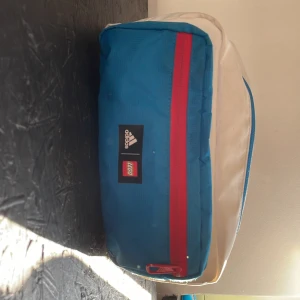 Adidas Lego magväska - Hej! säljer en stor Adidas Lego magväska med ett stort fack och ett litet. Skick 8/10 skriv om ni vill ha fler bilder!