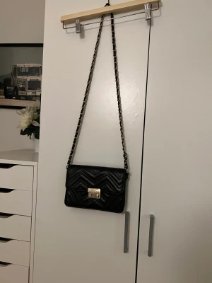 Handväska - Svart mellanstor handväska med gulddetaljer perfekt för utekvällar etc. Den är i bra skick utan fläckar eller annat.