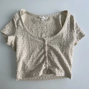 H&M topp - H&M topp med små hål och knappar, lite som en kortärmad tunn kofta.