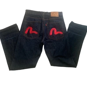 Evisu Jeans  - Hej säljer nu de evisu Jeans. De har rött evisu märke på bakfickorna.  Evisu märket är i ett cool palljet material. Midjemått: 44 cm innerbenslängd: 88cm benöpning:22cm längd från midja 112cm Skriv om ni undrar över något särskilt eller är intresserade.