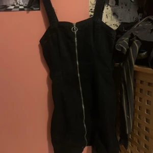 Svart klänning  - En kort svart klänning som slutar innan knäna. En kjedja som går ner i mitten fram