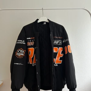 Bomberjacka Race H&M - En svart bomberjacka med orangt tryck från H&M. Knappt använd, väldigt oversized fit 