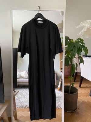 Oanvänd svart klänning från COS - Säljer min klänning från COS då den aldrig riktigt kommit till min användning. Den har jättefina armar som gör att det blir lite av en cape form, slitsar på båda sidorna av benen och en slimmad fit (iaf på mig). Är storlek S men passar även M