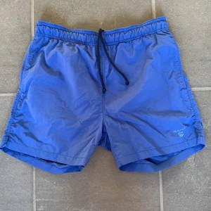 GANT badbyxor - Ett par blå snygga Gant badbyxor som jag säljer för dom har blivit för små för mig. Det är en liten ”repa” på baksidan som knappt syns. Det finns 2 framfickor och en bakficka