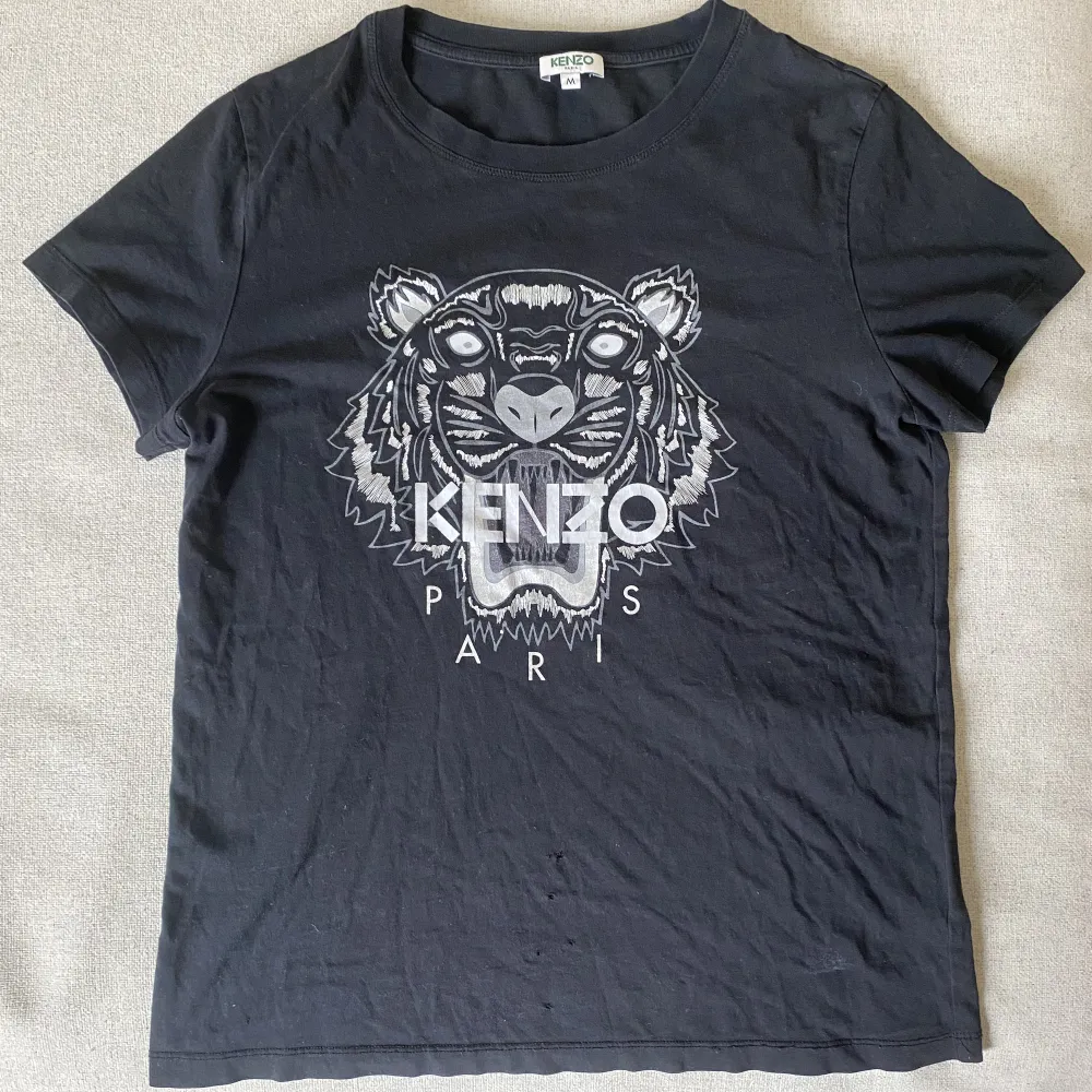 Svart Kenzo t-shirt den är liten i storleken skulle jag säga.  Det är även några få hål längst ner på tröjan, därav priset. Har man tröjan instoppad framtill så syns det inte, annars är den i toppskick!  Köparen står för frakten✨. T-shirts.