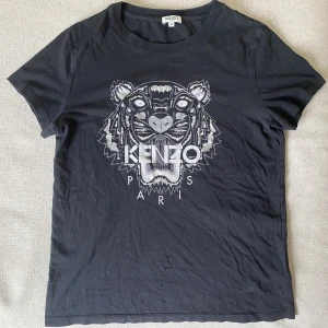 Kenzo t-shirt - Svart Kenzo t-shirt den är liten i storleken skulle jag säga.  Det är även några få hål längst ner på tröjan, därav priset. Har man tröjan instoppad framtill så syns det inte, annars är den i toppskick!  Köparen står för frakten✨