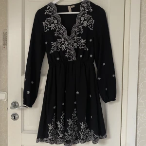 Svart klänning med vita broderier - En söt kort klänning som använts på nyår en gång, bra skick. Väldigt fina detaljer och ganska urringad. Klänningen är i storlek 34 men passar även 36. Säljer eftersom den inte riktigt är min stil och kommer därför inte till användning.