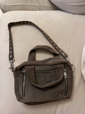 Nunoo väska  - Grå nunoo väska i mockamaterial. Finns inte kvar i sortiment. Använt men bra skick. Finns tillhörande längre band som är oöppnat