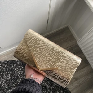 Väska  - En superfin handväska som endast är använd under en kväll! Inga skador eller defekter, som ny. Köptes för närmre 400kr och jag säljer för 100kr. 23,5 cm bred och 13 cm hög. Axelremmen går att ta av och sätta på enkelt.