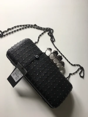 Svart väska med små nitar - Snygg svart väska med dödskallar. Kan användas med eller utan axelrem.  Nyskick, aldrig använd. 