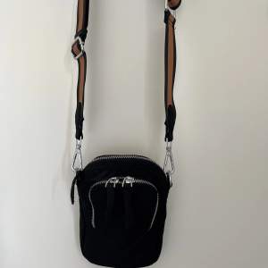Snygg svart nylon väska i märket Adax. Liten smidig perfekt för mobil plånbok nycklar. Med ställbar canvasrem. Väskan är i nyskick! Mått H19  B13 D3
