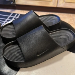 Nike tofflor - Calm slide - Säljer dessa näst intill oanvända nike tofflor. Säljer pga att min bror köpte precis likandana som vi kan dela på. De är i nyskick och väldigt sköna. Strl 44, jag bär 42,5 i alla mina skor så de är väldigt små i storleken. 