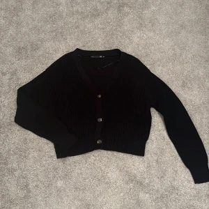 Stickad kofta - Stickad svart kofta, svarta knappar med bruna/vita detaljer, bra skick, använd ett par gånger, inga skador, lite kort i modellen