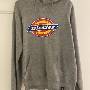 Dickies hoodie - En grå dickies hoodie i storlek S! Nypris är 750kr. Den är använd vilket man ser på bild 2 (tyget har börjat spricka vid halsen samt motiver med). Frakt tillkommer!