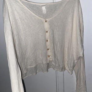 Cardigan  - En kräm vit färgad cropped cardigan i ett tunnare material med bruna knappar. Storlek L men passar fint på storlek M. 