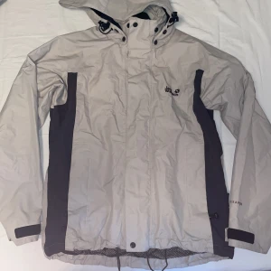 Vindjacka  - Snygg beige vindjacka från Jack Wolfskin i storlek S. Avtagbar luva med dragkedja.