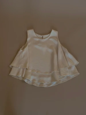 Upcycled Silk Peplum Top - Flowy Silk Tank with Double Skirted Hem. Single Button Closure in Back. Made with Deadstock Designer Heavy Silk Fabric. Excellent Condition. Model is 160cm (5”3) and generally fits XS/S.   40 CM/ 15.7 IN Length 28 CM/ 11 IN Shoulders 76 CM/ 29.9 IN Chest