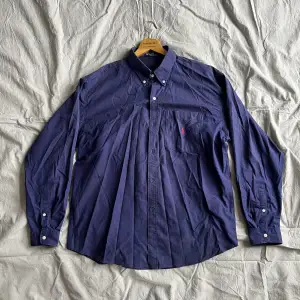 Begagnad mörkblå skjorta som utger sig för att vara Ralph Lauren men är troigtvis en kopia. Skön hur som helst.  100% bomull. XL