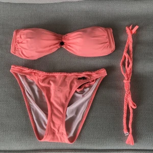 Korallfärgad bikini - Bandeaubikinitopp (med tillhörande band som man kan ta av/på) och matchande bikinitrosor från Odd Molly i snygg korallig färg. Storlek 1 i både topp och trosor, vilket motsvarar en S. 150kr per del + frakt, eller 250kr+frakt för båda ❤️