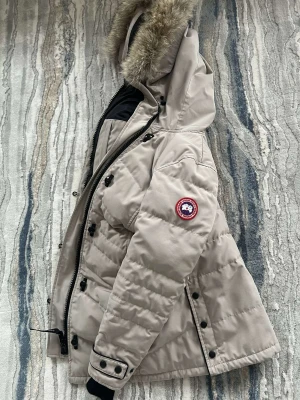 Canada goose jacka - Denna jackan är köpt för ett år sedan och har endast använts en vinter, jackan är i ny skick och är ga ska hållbar. Varm, vattentålig, matchande till allt. Den är i stolen Xs, för liten på mig. Det är den nya modellen från canada goose