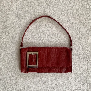 Liten vintage väska - Röd liten axelväska i glansigt material och med silverdetaljer, originellt från Kappahl! Sliten i lädret lite överallt 🖤