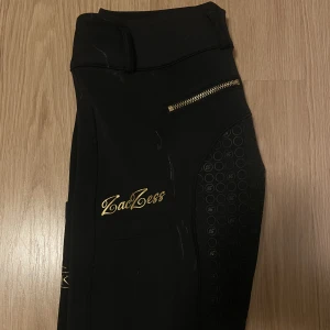 Ridbyxor från Zaczess - Svarta ridbyxor med gulddetaljer från zaczess. Storlek XS, full grip, Säfva ridklubbs logga på mobilfickan. Fint skick, bilder hur de ser ut på kan skickas vid intresse💗