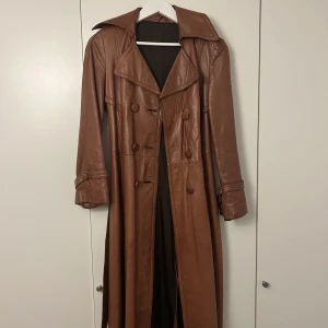 Lång brun skinnkappa - Säljer min supersnygga långa skinnjacka i brunt. Vintage från kungliga hovleverantören Zielfeldt Göteborg. Fint skick yttre sida men invändigt har den slitage vid armhålorna, inget som påverkar utseendet utåt. Storlek 38.