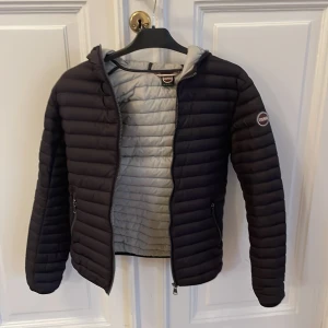 Colmar jacka  - Colmar jacka storlek 14, 166 cm. Lättviktsdunjacka svart, med grå insida och luva. Knappt använd. Väldigt användbar under vår och höst. Superfin!