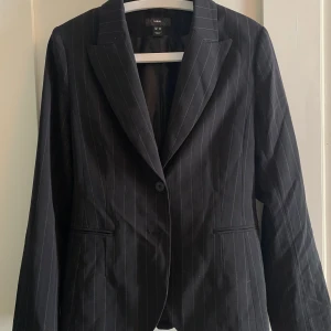 Svart kavaj  - H&M kavaj med bruna ränder. Två extra knappt finns. Yttertyg 62% polyester 32% viskos 6% elastan. Foder 100% polyester 