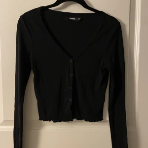 Kofta - En kofta som är croppad och tajt som kan användas som topp. Har lite volanger längst ner.