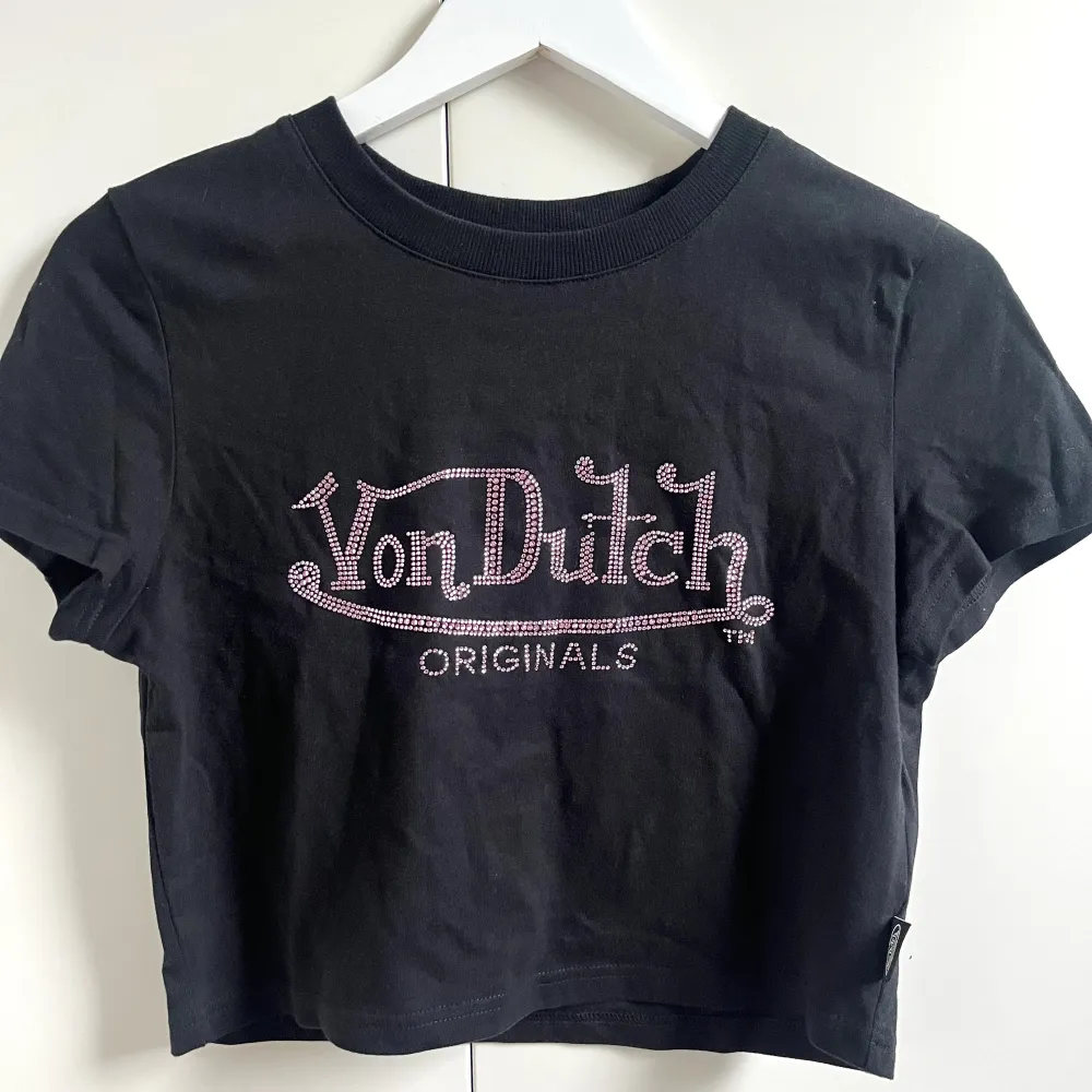 Säljer denna croppade t-shirt från Von Dutch. Köptes i början av 2023 från Nelly.com. Använd max 3 gånger. Skicket är bra men några strass stenar har åkt. Storleken är M, står dock L i men ska vara M. Jag är en Xs/S för ville ha den mer lös i passformen. . T-shirts.