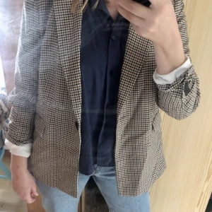 Kavaj - Klassisk kavaj med enkelt mönster. Höstig. Kan kläs upp och casual. Lite figursydd. Storleken är 46 men den är liten. Den sitter bra och lite ledigt på mig som har st 42 (är 171 cm lång och väger ca 70 kg). Nyskick.