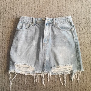 Fang GuiXiang - Super snygga jeanskjol med tjänor detalj. Den är helt nyskick och säljs för att ej kom till användning. Mått för kjolen är 36cm i midja och 39cm i längden. 