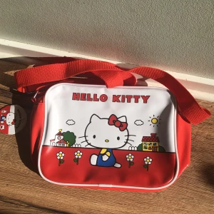 Hello Kitty väska  - En hello kitty axelremsväska (justerbar!) Aldrig använt, lappen är till o med kvar vilket syns på sista bilden❤️ HÖGSTA BUD: 80 KR 