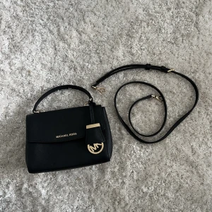 Äkta MK-väska - Säljer då den ej kommer till användning.  Inga fel eller defekter.  Färg: Svart.  Stängs med magnet.  Tre ”fack” i väskan, varav ett stängs med dragkedja. Väskan har även ett fack på baksidan. 