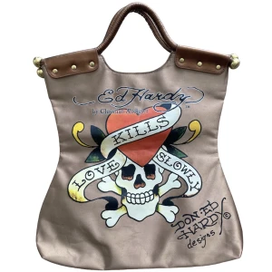 Ed Hardy Bag - Supercool stor väska med tryck från Ed Hardy!💋 Perfekt till sommaräventyr och stranden! Guld/koppar liknande färg! MÅTT: Bredd: minsta 34cm, högsta 41cm/ HÖJD- minsta 41cm, högsta 45cm! Är inte 100% säker på om den är äkta eller inte!💋