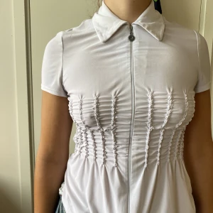 Zipped blus  - Stretchig vit blus med dragkedja heal vägen! Så fin modell med smock i midjan, men rätt använd! Syns i vitfärgande och stretchen är uttöjd. Men inget som stört mig när jag använt. Sitter nog bäst och tight på en 40/42 men som på bilden på en 38/40.