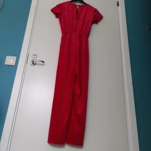 Röd Byxdress KappAhl Storlek 152 - Röd (ngt djupare nyans än bilden) byxdress med samhets liknande ribbat utförande på utsidanmed glitter trådar i. Storlek 152 från Kappahl  Obs, hund finns i hemmet   Fraktas enligt överenskommelse. Frakten bekostas av köparen.  PRISET GÅR ATT FÖRHANDLA