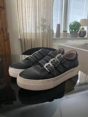 K.Cobler i skinn - Svarta sneakers med tre spännen på med nitar, vit sula sparsamt använda 
