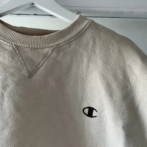 Champion sweatshirt Beige/cream  - En skön sweatshirt från champion i storlek L med lite baggy känsla och retro stuk, bruna detaljer som passar perfekt till det cream färgade. Sitter även perfekt baggy på mig som i vanliga fall har M. skriv gärna vid funderingar:) 