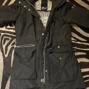 Röhnisch vinterjacka  - Som ny, inget att anmärka. Är använd kanske 1/2 gånger. Storlek 38. All Weather Parka från Röhnisch är en vind- och vattentät parkas med varm, lätt vaddering. Vattenpelare 10 000 mm och andasförmåga 10 000 g/m2/24h. Avtagbar, justerbar huva 