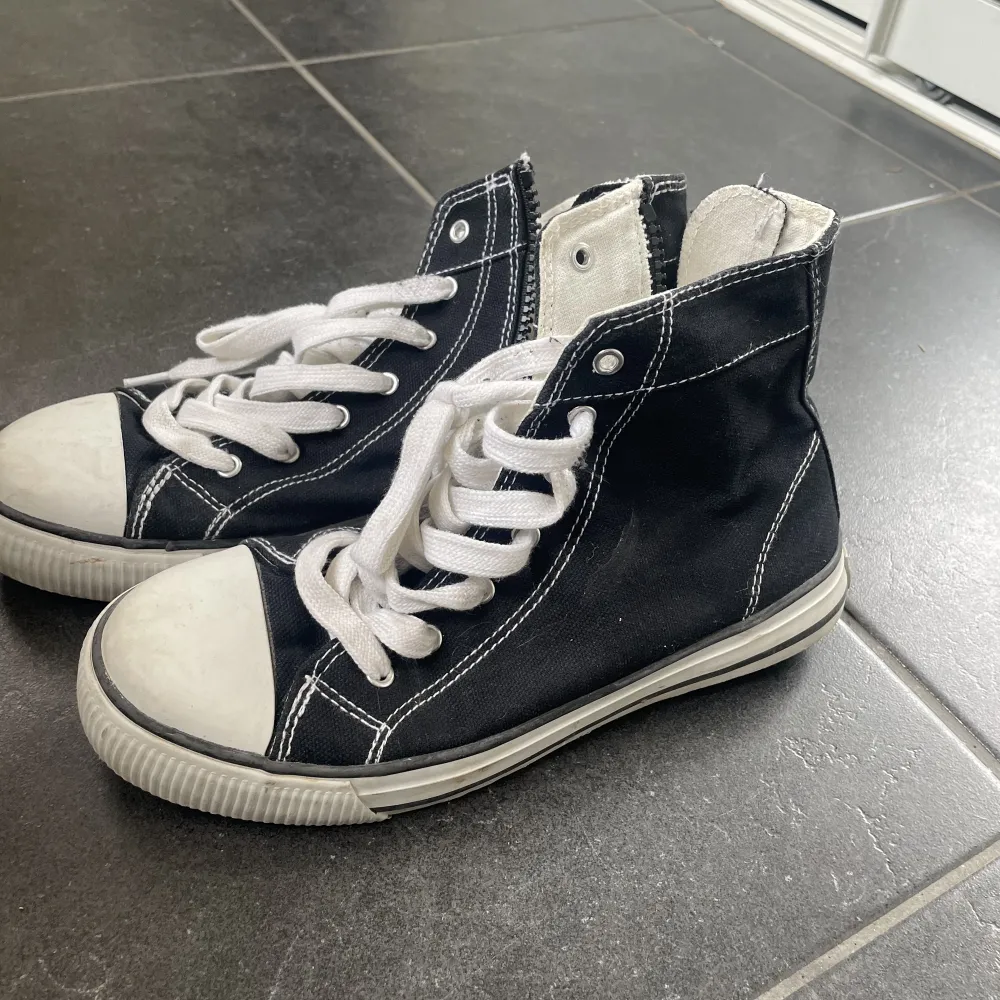 Fake Converse sneakers som är svarta med dragkedja på insidan och snörning upptill. Bra skick och liknas höga Converse mycket, särskilt när man har byxor och bara toppen syns. . Skor.