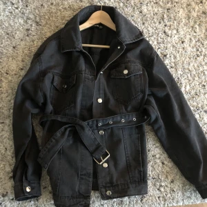 Svart jeansjacka Prettylittlething - Så snygg jeansjacka,svart med grå ton från Pretty little thing. Bälte i midjan. Strl S men passar även M