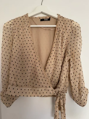 Kort beige prickig topp - Kort beige och svart prickig topp med långa puffärmar och knytning. 