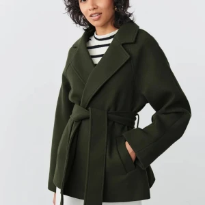 Kort kappa - En helt ny, oanvänd grön kappa från Gina Tricot. Den är i ett tjockt och varmt material.  Jag säljer den för att jag köpte fel storlek och hann inte lämna tillbaka den. Skulle säga att den är ”normal” i storleken. (Bild från hemsida) Finns på flera sidor