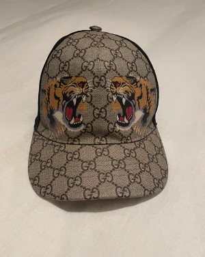 Guccikeps - Gucci keeps med två tigrar, aldrig använd och med köpet får ni kvittot och COA, och även påsen skulle det önskas.   Storlek M (58 cm) 