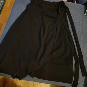 Svart omlottkjol  - Svart omlottkjol med band, tror man ska knyta en rosett eller nåt. Ca 75 cm lång, aldrig använd. SVÅR att fota!