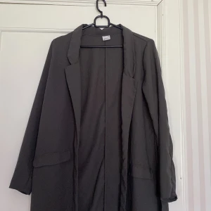 Blazer  - Lång mörkgrå blazer från ginatricot, storlek 34🤍 Den har slitt på båda sidorna💕 Köparen står för frakt!