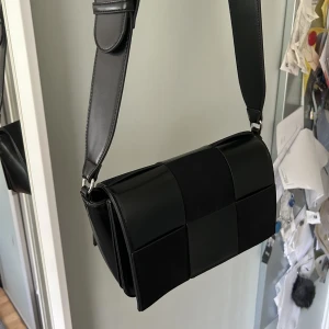 Svart handväska - Snygg svart handväska med mocka mönster framtill. Långt band så snygg att ha cross-over. Får plats med mycket! Bra skick